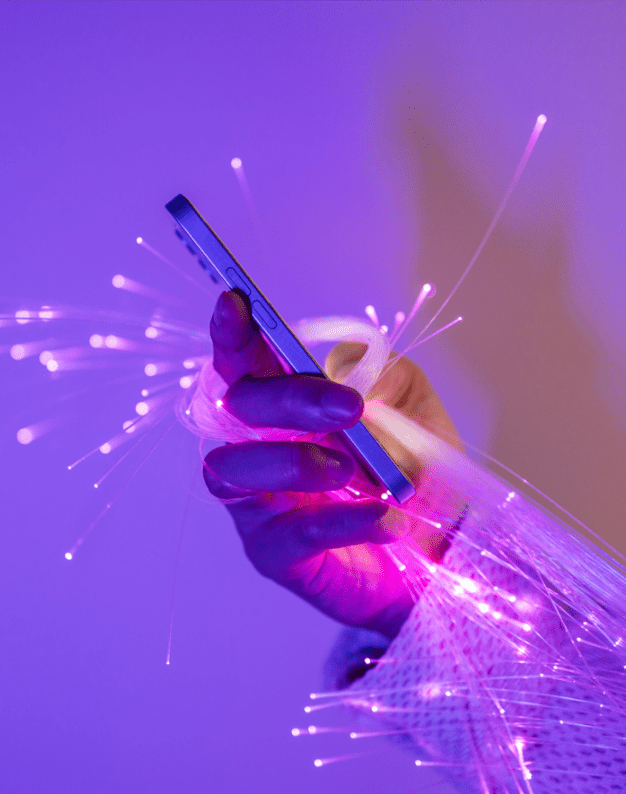 A hand holding a smartphone surrounded by bright, glowing fiber optic strands in a modern, tech-inspired setting with a purple background.