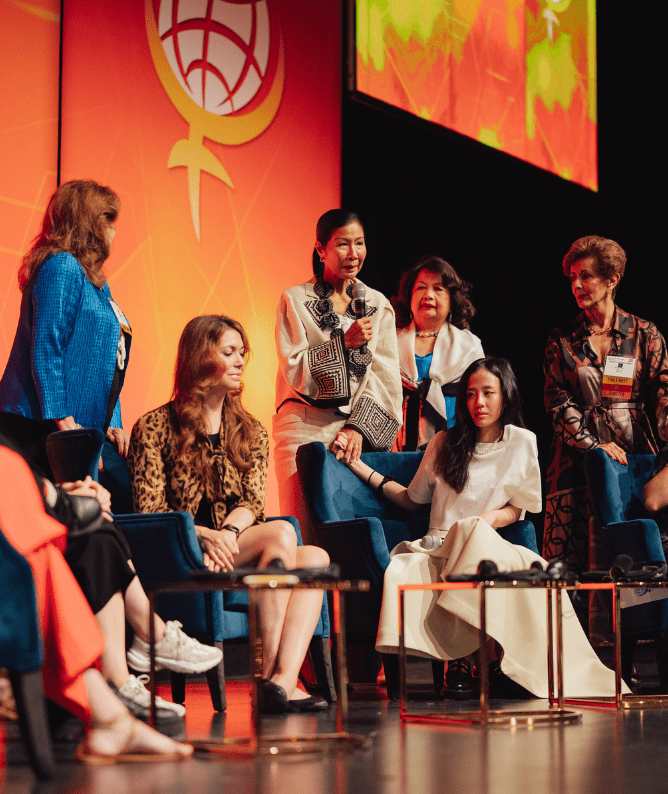 3 A diverse panel of women engaged in discussion at a conference, focusing on women's empowerment and leadership. The event features a vibrant backdrop with a global feminist symbol, showcasing a dynamic exchange of ideas among participants.