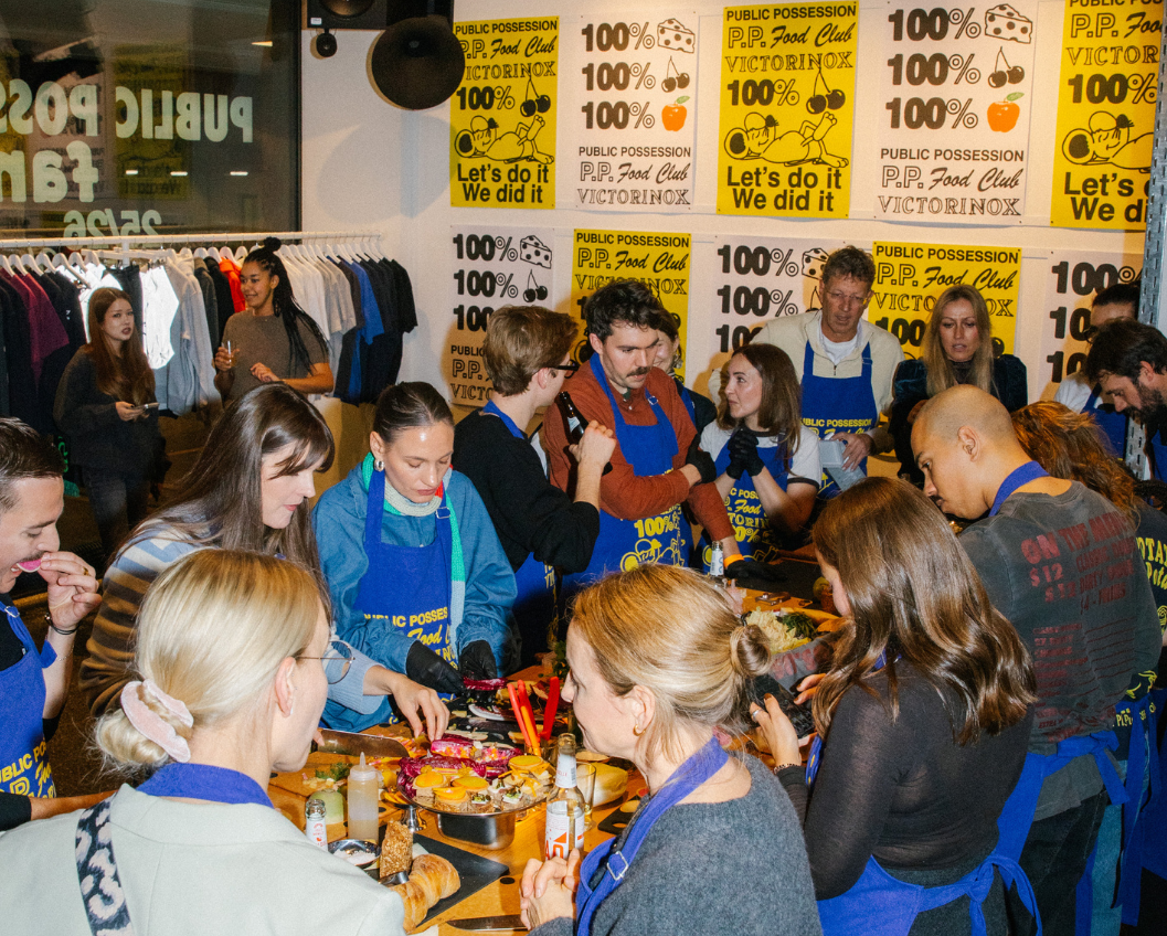 2 Group of people participating in a food event at Public Possession, wearing aprons and engaging in meal preparation, with a vibrant atmosphere and branded posters in the background.